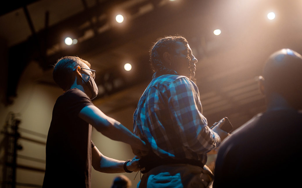 Man adjusts performer's mic under stage lights