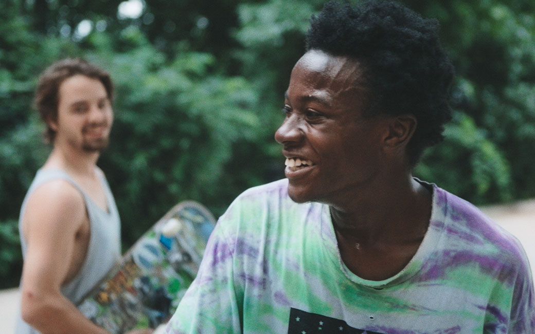 Film still with two men, one in background holding skateboard
