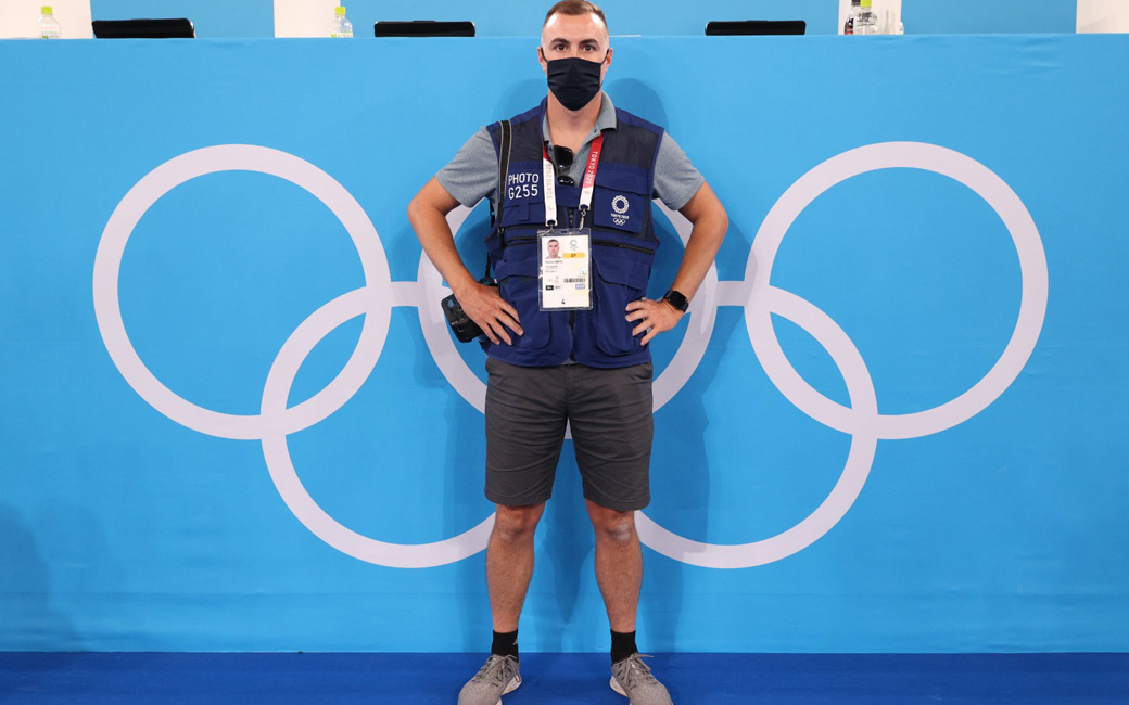 Patrick Smith, in a face mask, standing in front of the Olympics logo