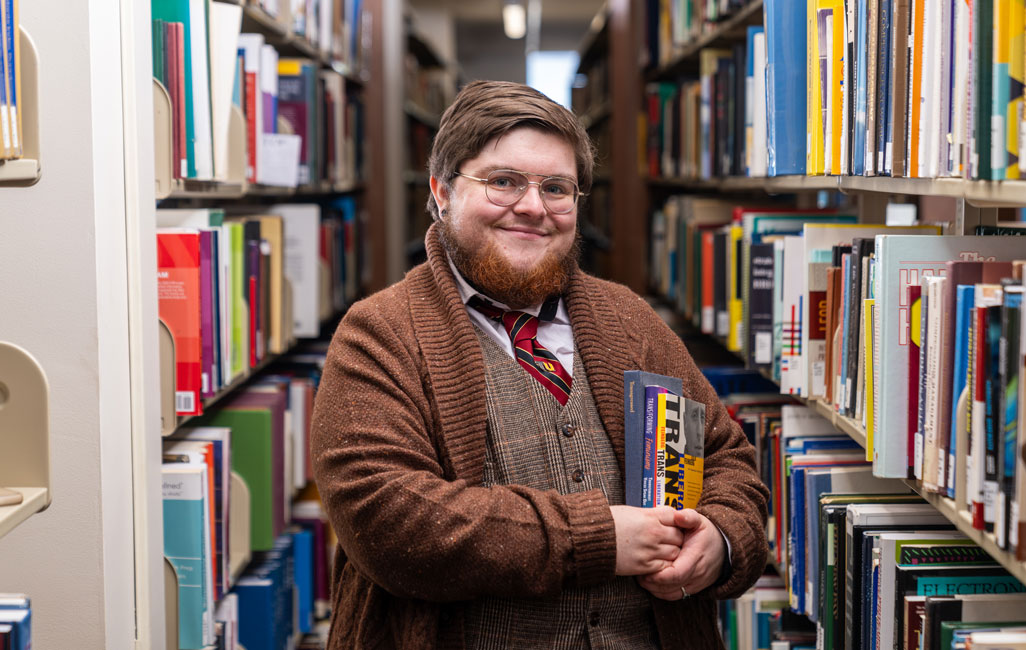 Person stands in library stacks holding books under their arm