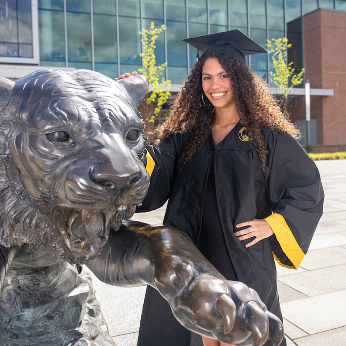 GIF of student in gradaution cap and gown posing by Tiger statue