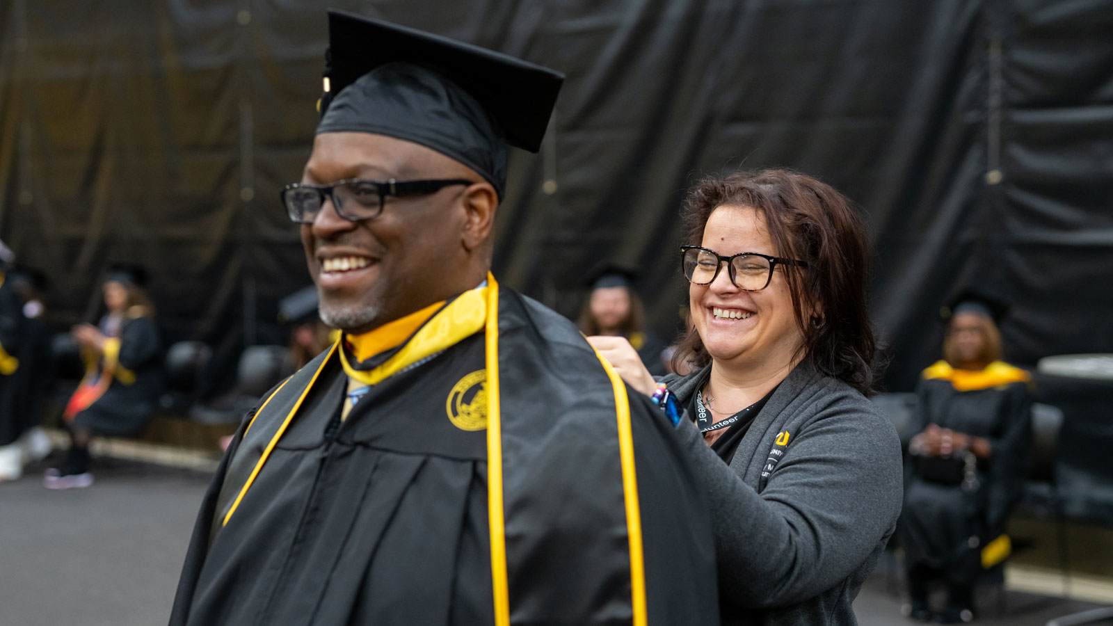 One staff volunteer helps a graduate adjust their regalia