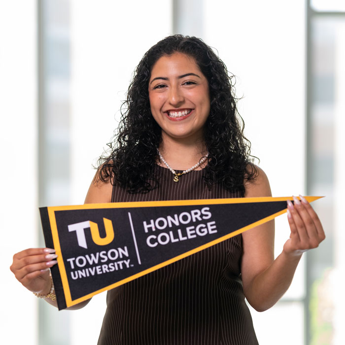 A smiling female alum holding an Honors College pennant in her manicured hands