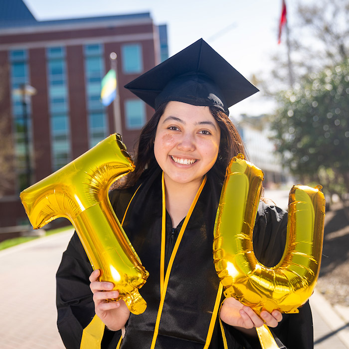 GIF of student in cap and gown holding TU balloons