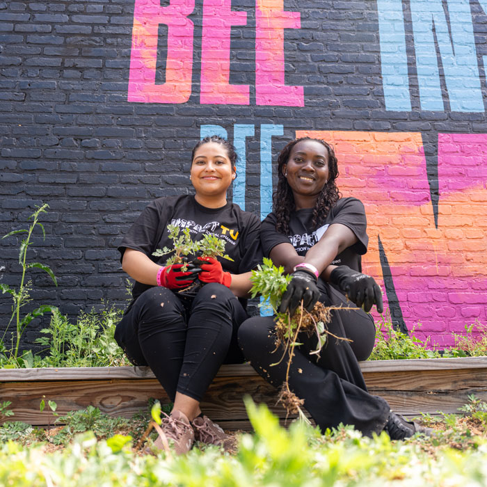 Two students hold greenery they weeded out of a local community space