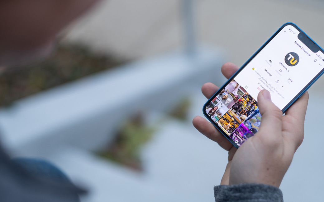 TikTok Person holding an iPhone shows TU's TikTok account on screen