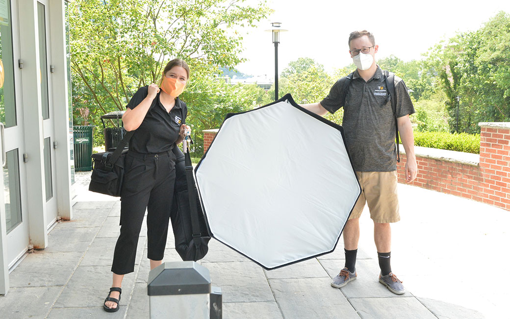 Photographers in face masks holding lighting equipment outside