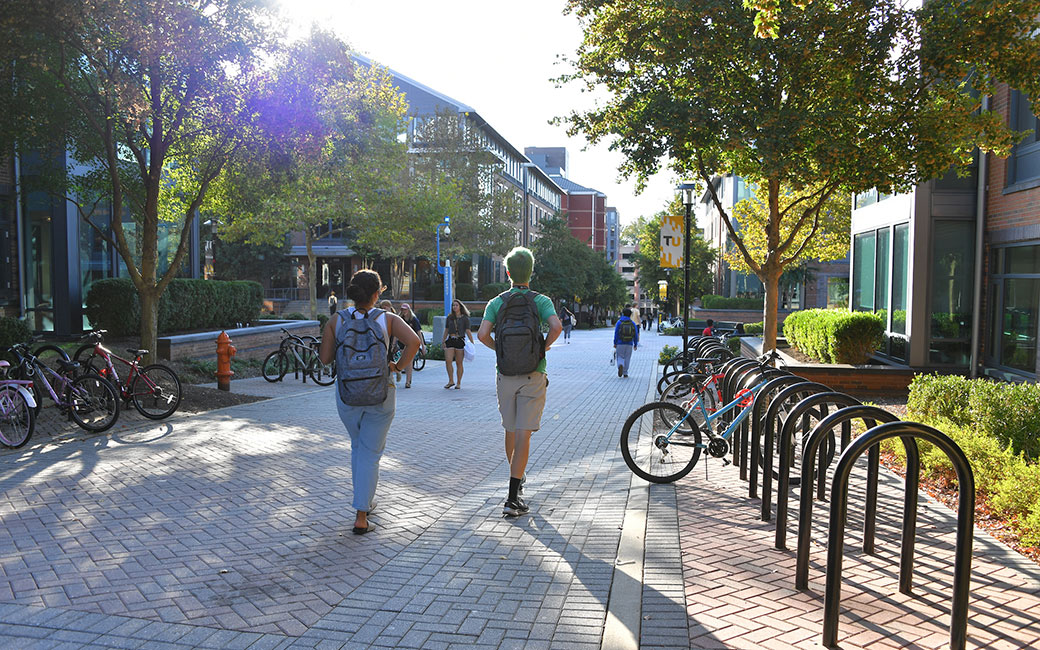 Students walk through West Village commons with sun flare