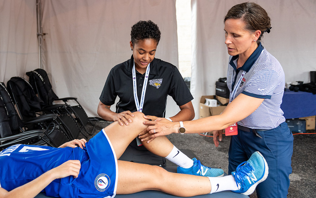 Two women touch leg of athlete on table