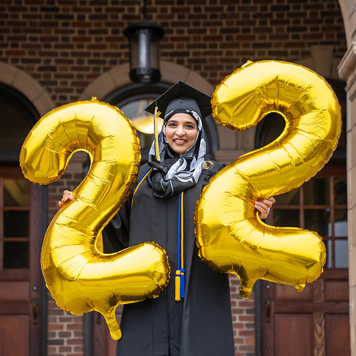 Student in cap and gown holding 22 balloons