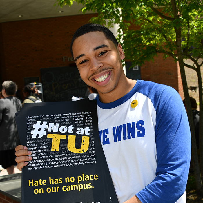 student holds a sign that reads #not at TU