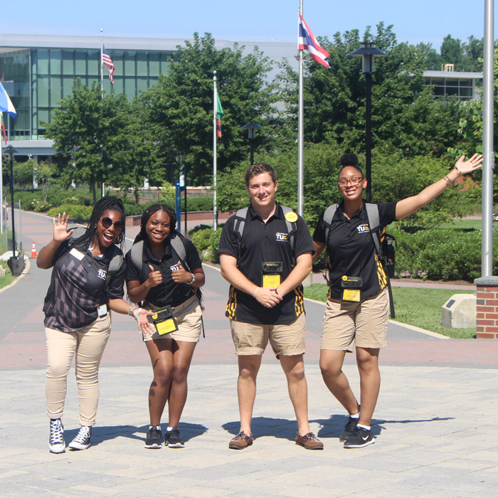four students in orientation staff uniform standing on walkway 