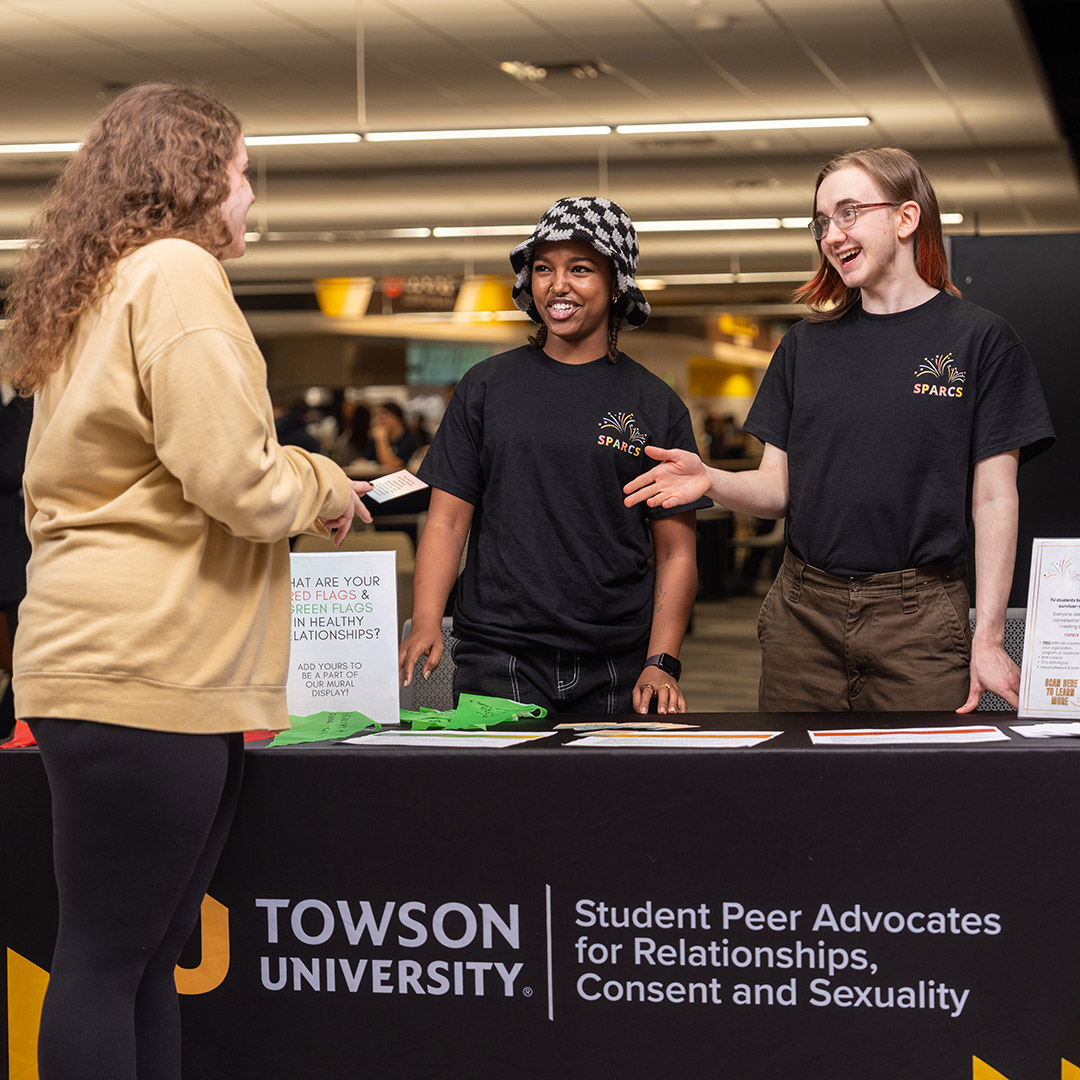Two peer educators behind a resource table talking to a student