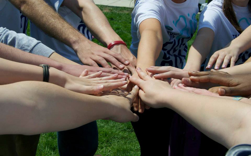 Circle of student hands reaching out and placed over each other