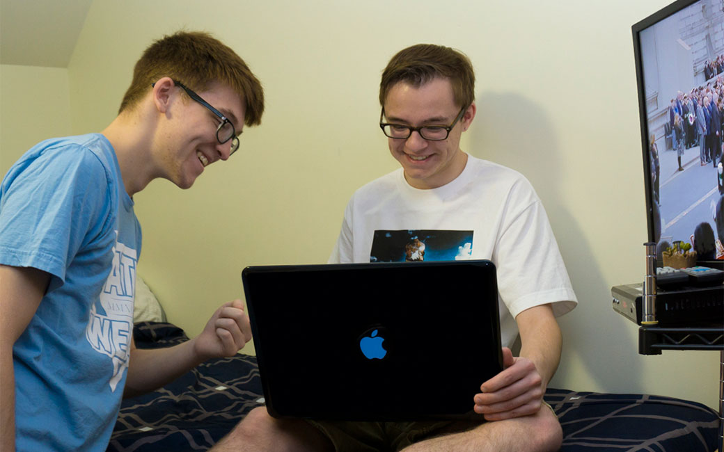 Two male students using a wireless laptop connection and watching cable TV in a residence hall room.